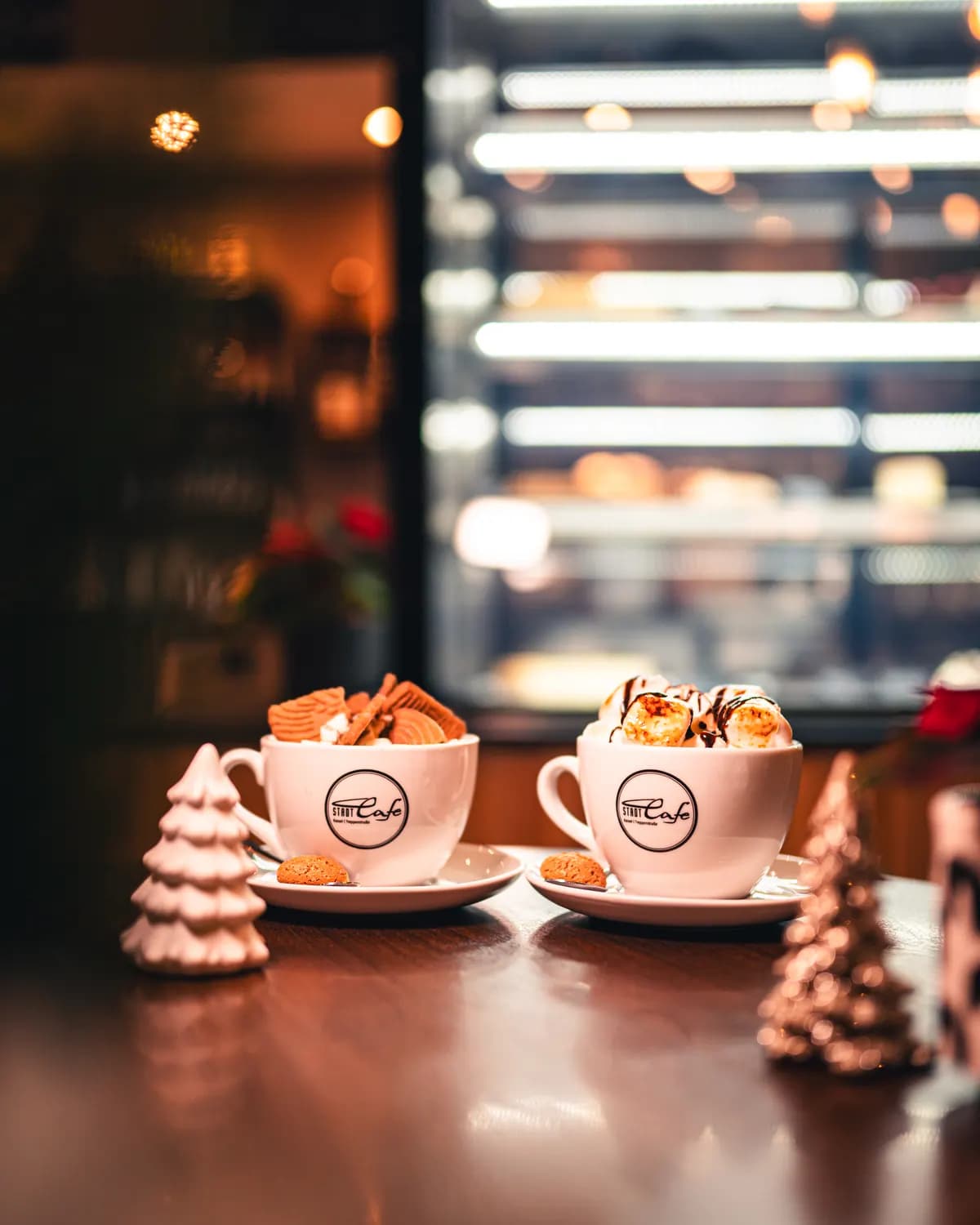 Zwei Tassen heiße Schokolade mit Sahne im Stadtcafe, daneben kleine Weihnachtsbäume